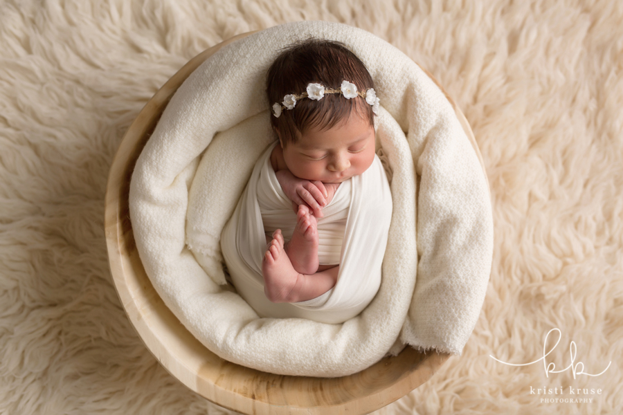newborn baby girl wrapped in white swaddle laying in wooden bowl on