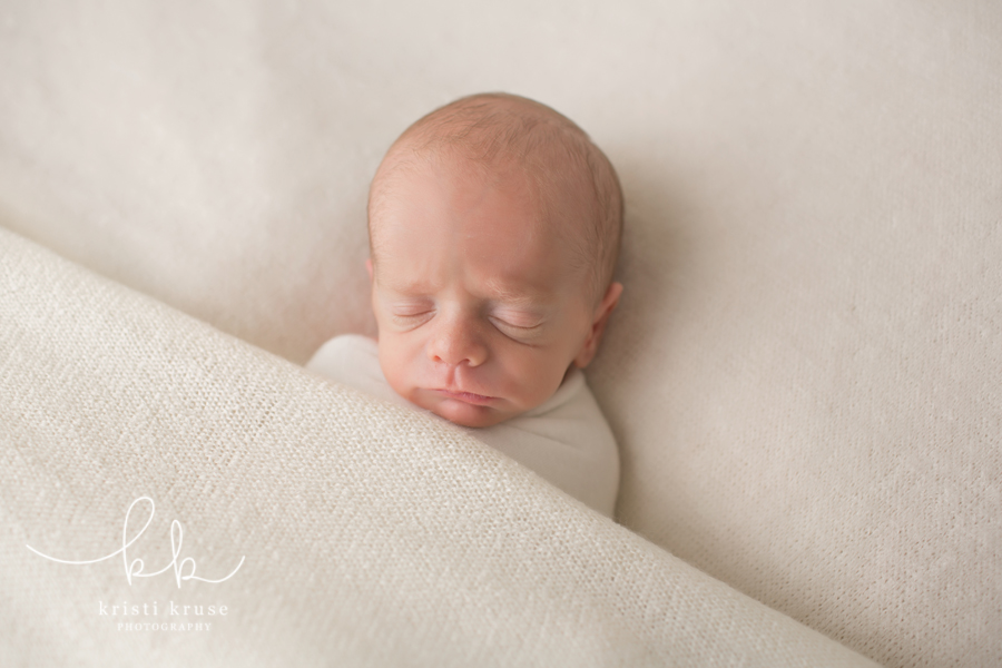 Newborn baby boy all tucked in and sleeping in a white swaddle and blanket