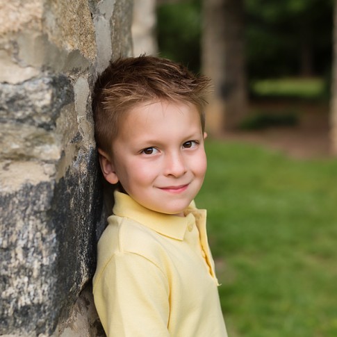 5 year old boy leaning against stone wall looking at camera