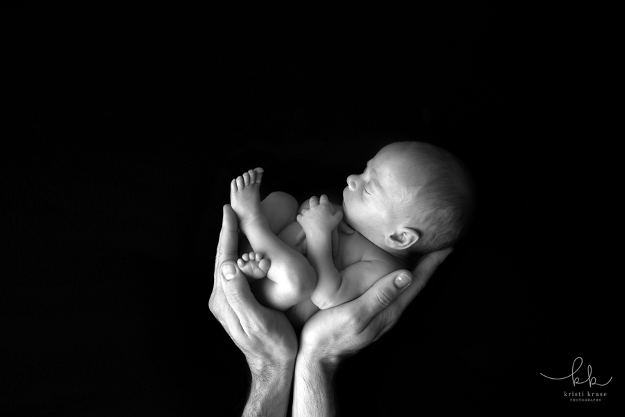 Black and white art image of tiny newborn baby boy in his father's hands.  