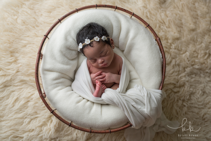 newborn baby girl wrapped in white swaddle laying in a basket with white blanket