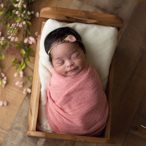 newborn girl wrapped in pink swaddle lying in small bed with flowers