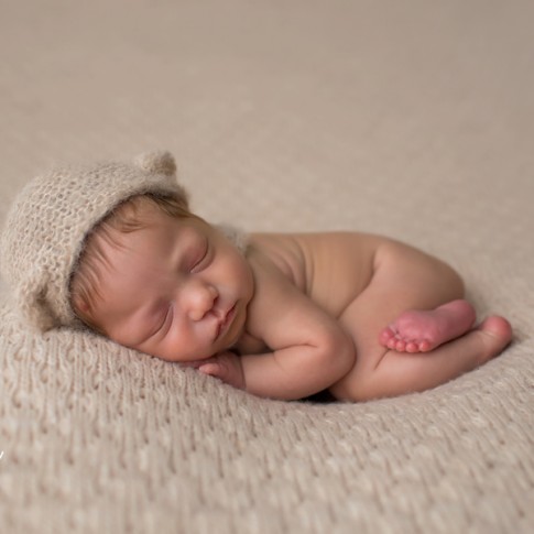 Newborn baby girl in bear hat on beige blanket