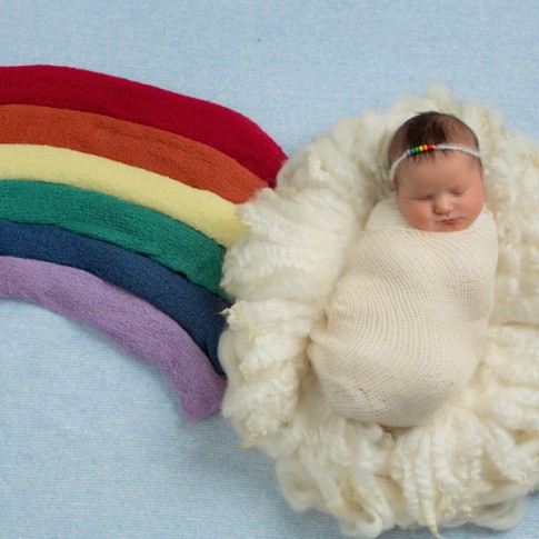 Baby girl in cloud of white fluff with rainbow