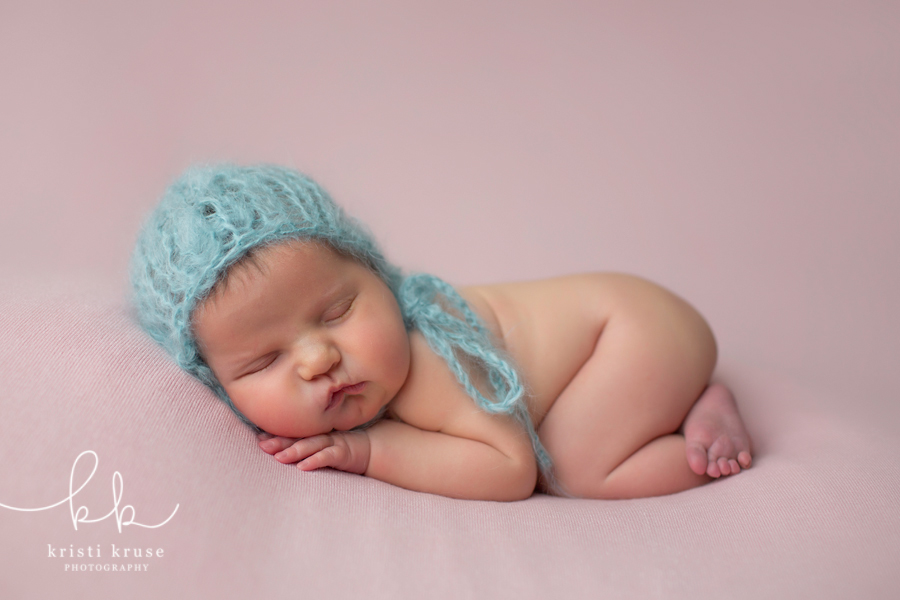 Baby girl on pink blanket with blue bonnet