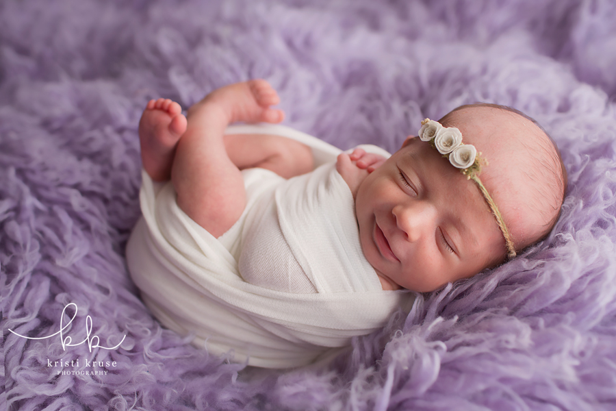 newborn baby girl smiling while laying on a purple flokati