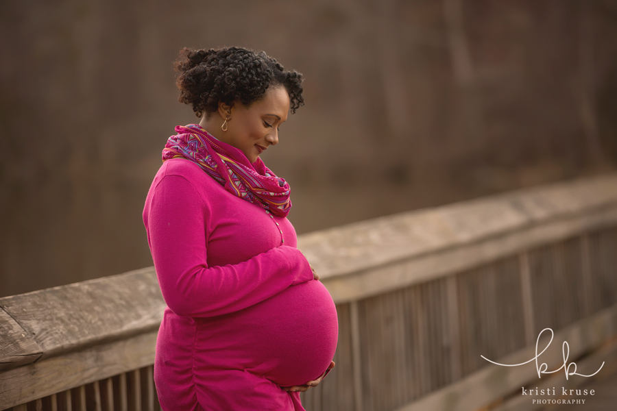 Pregnant woman on wooden bridge standing sideways holding her belly