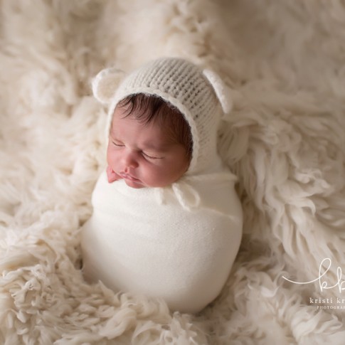 newborn baby girl wearing white knit bear hat and wrapped in white wrap