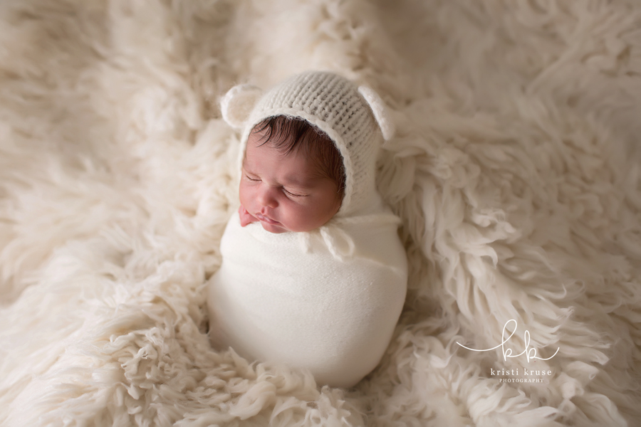 newborn baby girl wearing white knit bear hat and wrapped in white wrap