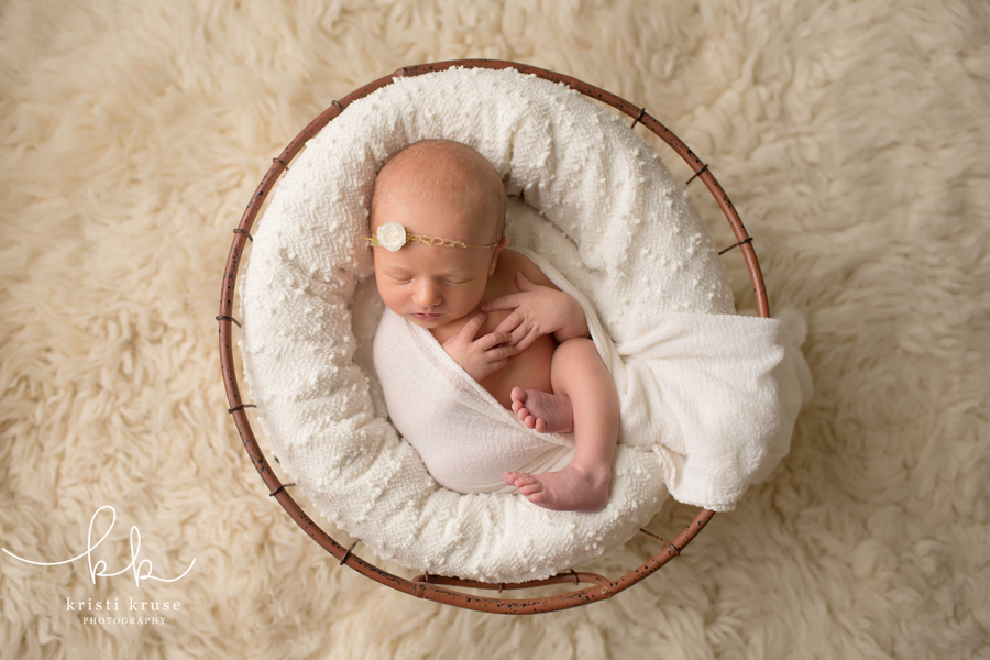 newborn baby girl wrapped in white swaddle lying in white basket on white rug