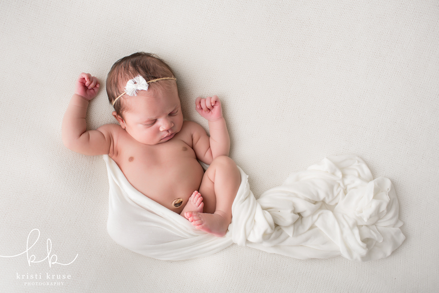 baby girl lying on her back on white blanket with with matching wrap and bow