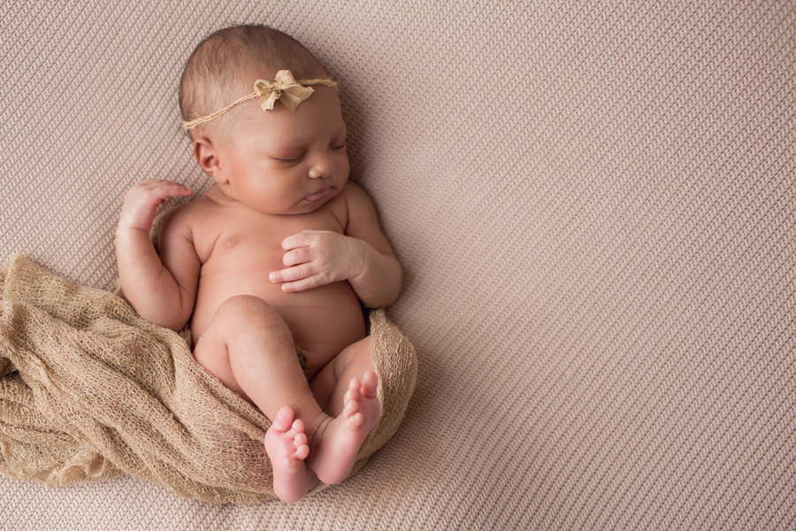 Baby girl with brown bow and wrap laying on brown blanket