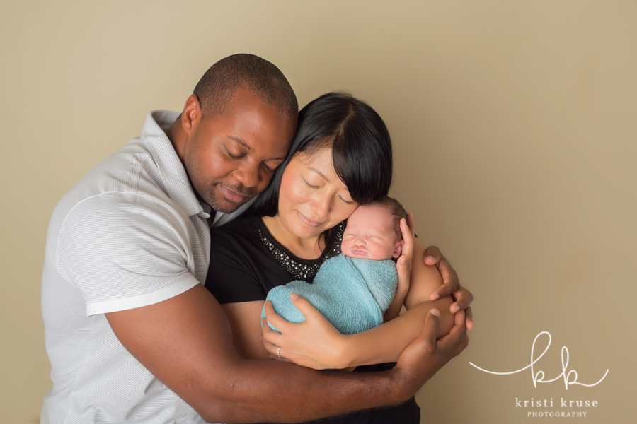 Mother holding newborn baby close to her face while Dad wraps his arms around mother and baby