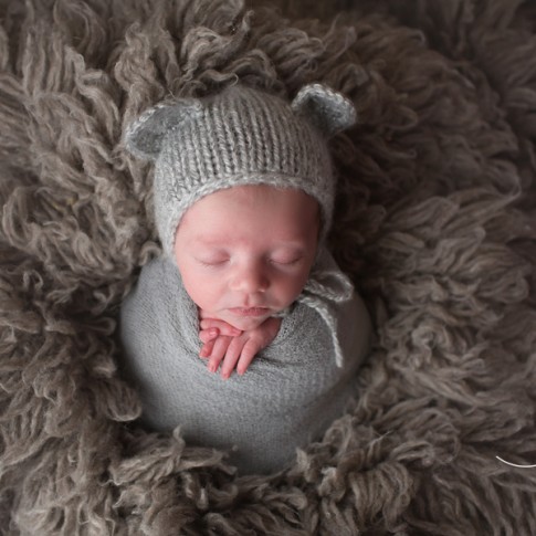 Newborn baby boy wrapped in gray wrap with gray knit bear hat