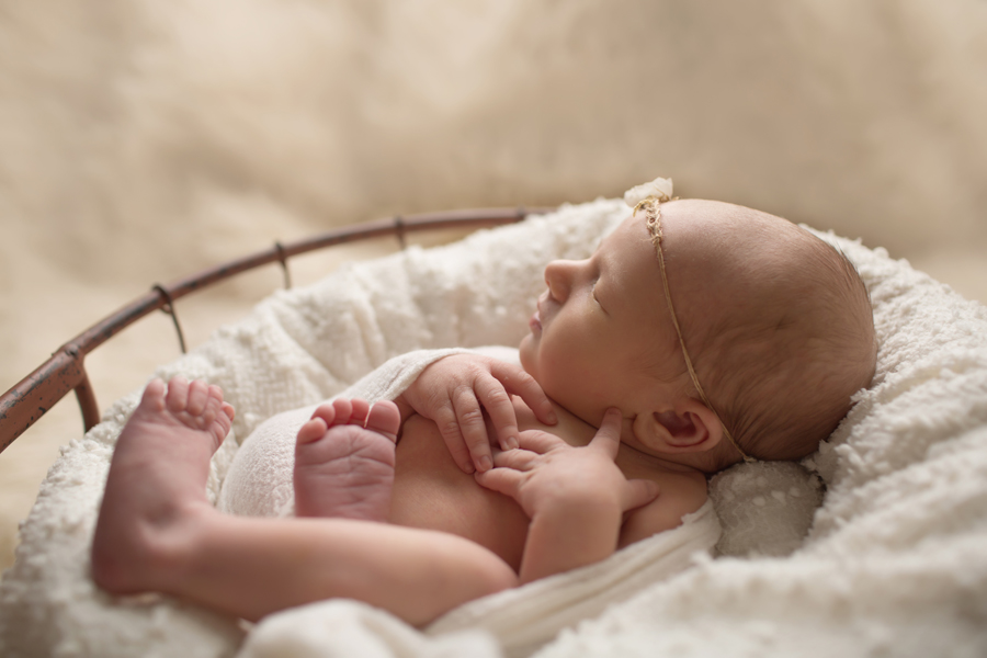 Side profile of newborn baby girl in white basket on white rug