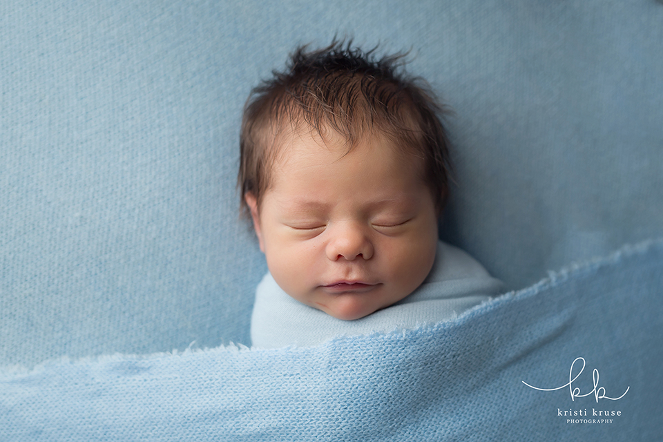 newborn baby boy with full head of hair laying on blue blanket