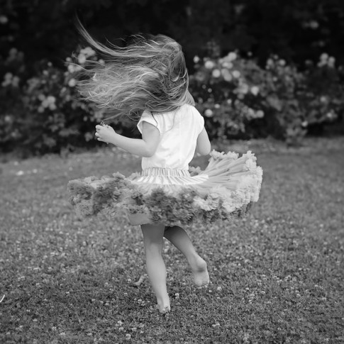 3 year old girl wearing tutu twirling in the grass