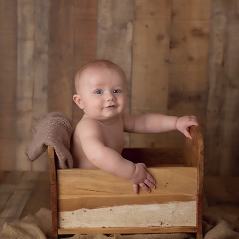 6 month old baby boy sitting in wooden prop bed