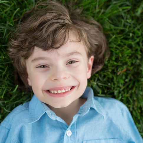 7 year old boy wearing a blue button down shirt lying on grass looking at camera