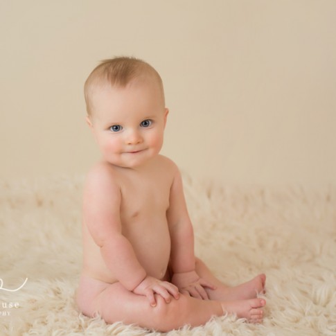 6 month old blue eyed baby boy sitting on cream rug